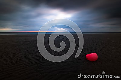 Orange buoy at the beach of Amrum island Germany during low tide with glowing dramatic sky and dark stormy clouds at sunset Stock Photo