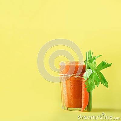 Orange carrot juice with carrots, celery on yellow background. Square crop. Fresh vegetable smothie in glass. Copy space Stock Photo