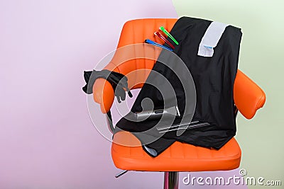 orange chair against the wall, for the hairdresser, with a set of tools for cutting, with Cape and clips. Stock Photo