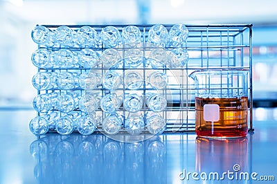 Orange chemical solution in science beaker and glass test tube in metal rack in education blue laboratory background Stock Photo