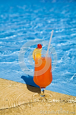 Orange cocktail stands on edge of pool. Stock Photo