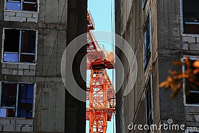 Orange construction tall crane between residential buildings under construction illuminated by early morning sunlight. Stock Photo