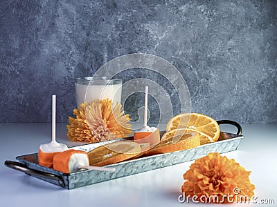 Orange Creamsicle cake pops arranged on a rustic metal tray with fresh sliced oranges and a glass of milk with orange flowers and Stock Photo