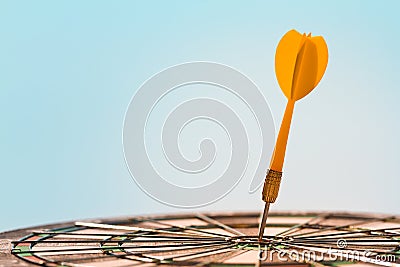 Orange dart arrow hitting bulls-eye in center of dartboard on blue sky background Stock Photo