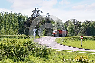 Orange Dump Truck moves on road on hill in green grass Stock Photo