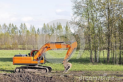Orange excavator on the background of a meadow and trees Stock Photo