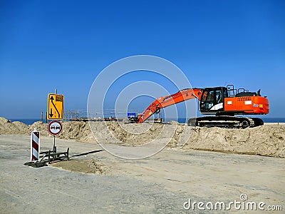 Orange excavator on pile of sand with road signs on construction Stock Photo