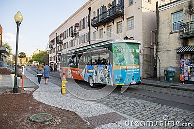 An orange and green trolley bus from Old Town Trolley driving on River Street with shops and restaurants and people walking Editorial Stock Photo