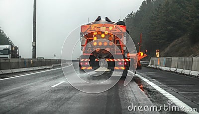 Orange highway maintenance gritter truck spreading de-icing salt, crystals dropping on the ice covered asphalt road during Stock Photo