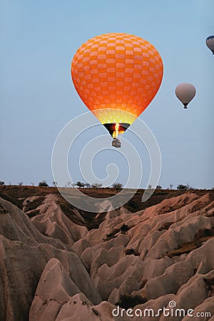 Orange Hot Air Balloon Flying In Sky Above Rocks In Nature Stock Photo