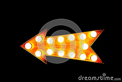 Orange illuminated display arrow sign with light bulbs against a seamless black background Stock Photo