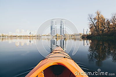 Orange kayak sailing towards modern buildings on the waters of Dnipro river in Kyiv, Ukraine Stock Photo