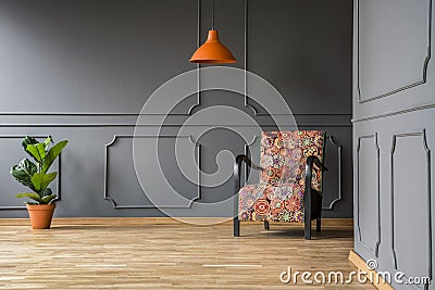 Orange lamp above patterned armchair in grey living room interior with plant. Real photo Stock Photo