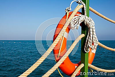 Orange lifeline and sea ropes on the background of the sea and blue sky. Marine ropes and life preserver hanging on a green post o Stock Photo
