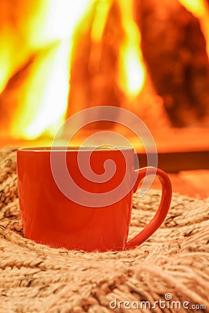 Orange mug for tea or coffee; wool things near cozy fireplace; w Stock Photo