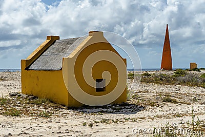 Orange obelisk with yellow slave huts on the old salt production plantation, Bonaire Stock Photo