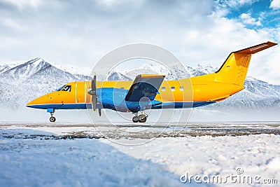Orange passenger turboprop aircraft on the winter airport apron on the background of high scenic mountains Stock Photo