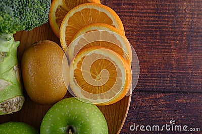 Orange pieces, apple, kiwi, and Broccoli on a wooden plate Stock Photo