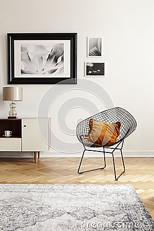 Orange pillow on a black, industrial net chair by a white wall with gallery of mock-up pictures in an elegant living room interior Stock Photo