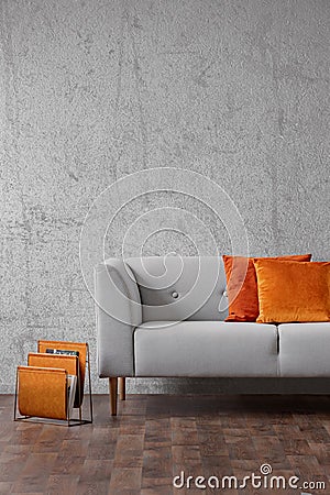 Orange pillows on grey settee in living room interior with concrete wall and wooden floor. Real photo Stock Photo