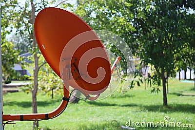 Orange satellite dish for receiving signal next to the roof of the house for good signal reception Rural forest background Stock Photo