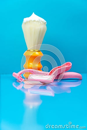 An orange shaving brush at the tip smeared with shaving foam next to pink disposable razors against a light blue background Stock Photo