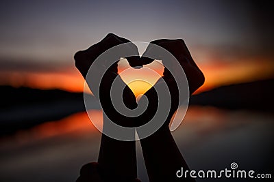 Female hands in the form of heart on twilight and orange sky. Horizontal view Stock Photo