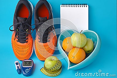 Orange sneakers, diary notebook, glucometer, measuring tape and fruits on a blue background Stock Photo