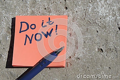 orange sticker with the words do it now and a pen on a concrete surface Stock Photo