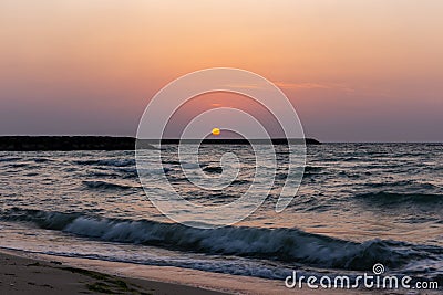 Orange sunset with golden reflections in sea waves, Al Hamriyah beach in Umm Al Quwain, UAE Stock Photo