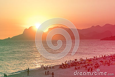Orange sunset by the ocean in Piratininga, Niteri, with sun dipping behing the Gavea Stone in Rio de Janeiro. A beach full of peop Stock Photo