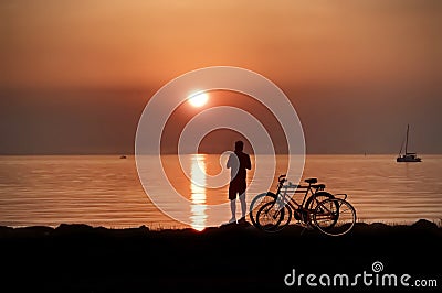 Orange sunset at promenade woman with bike relaxing and watching pink cloudy evening sky sun down gold hour at sea nature landsc Editorial Stock Photo