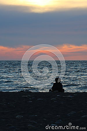 Orange sunset on the sea, the silhouette of a man on the background of the sunset. A girl sits on the beach at sunset Stock Photo