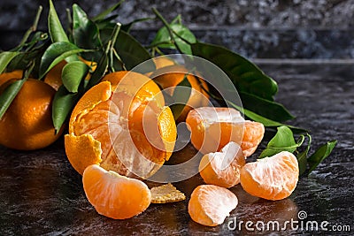 orange tangerines with green leaves on dark background. Peeled mandarin slices Stock Photo