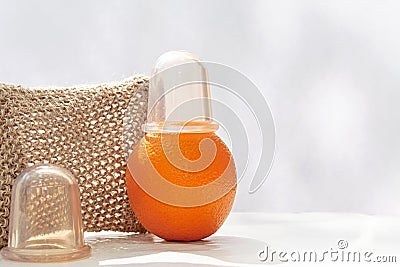 An orange with a vacuum can at the top is on the table against the backdrop of a mesh washcloth made from natural fibers Stock Photo