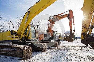 Orange and yellow powerful crawler excavators standing at a construction site against the backdrop of the sun Stock Photo