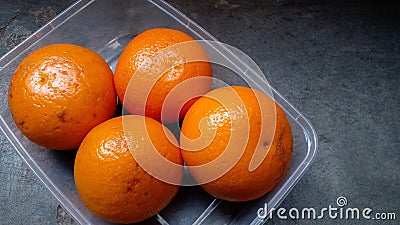 Oranges placed in plastic container on a cement bench. High angle view. Fresh fruit. Stock Photo