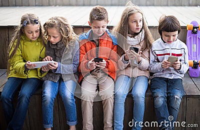 Ordinary children playing with the phone on bench outdoors Stock Photo