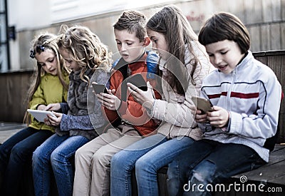 Ordinary children playing with the phone on bench outdoors Stock Photo