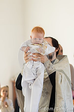 Orenburg, Russian Federation-2 Aprel 2019. Orthodox priest holding a baby during the baptism ritual Editorial Stock Photo