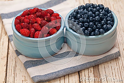 Organic berries bilberry and strawberry in blue bowls on wooden background, healthy eating concept Stock Photo