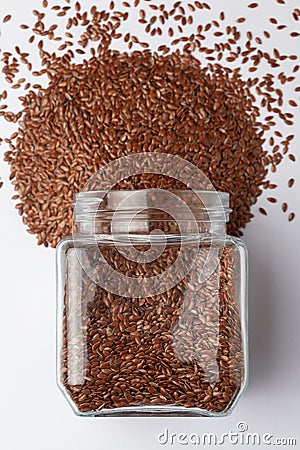 Organic Brown flaxseeds Linum usitatissimum or linseed, spilled and in a glass jar, Stock Photo