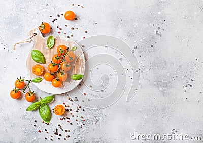 Organic Cherry Orange Rapture Tomatoes on the Vine with basil and pepper on chopping board on stone kitchen background. Space for Stock Photo