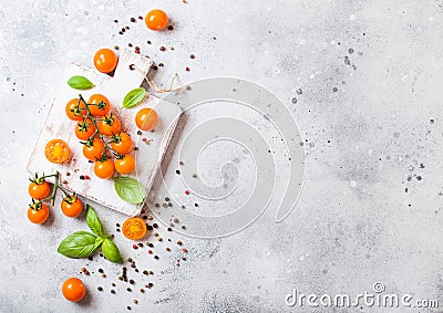 Organic Cherry Orange Rapture Tomatoes on the Vine with basil and pepper on chopping board on stone kitchen background. Space for Stock Photo