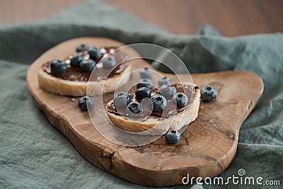 Organic chocolate hazelnut spread with fresh blueberries on ciabatta slices on wood board Stock Photo