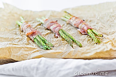 Organic green mini asparagus wrapped in bacon on wooden cutting Board. White background, top view. Stock Photo