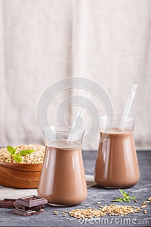 Organic non dairy oats chocolate milk in glass and wooden plate with oats seeds on a black concrete background Stock Photo