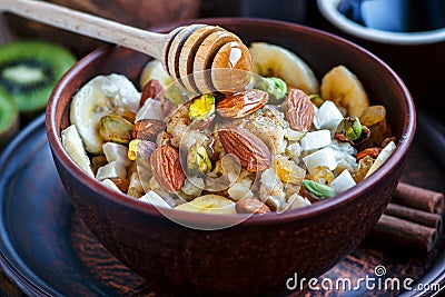 Organic oatmeal porridge with bananas, honey, almonds, pistachio, coconut, kiwi fruit, cinnamon, raisins in dark ceramic bowl Stock Photo