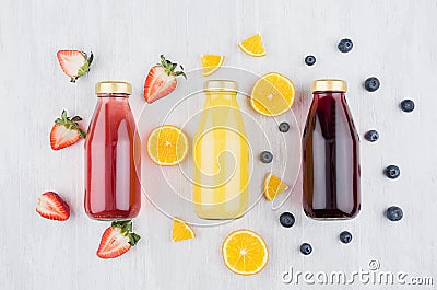 Organic yellow orange, pink strawberry and violet blueberry juices in glass bottles with fruit ingredients on white wood board Stock Photo