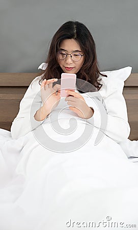 Oriental lady happily playing with mobile phone in bedroom Stock Photo